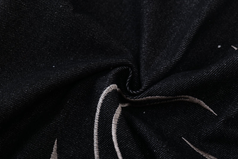 Close-up of dark denim fabric with light tribal embroidery stitching