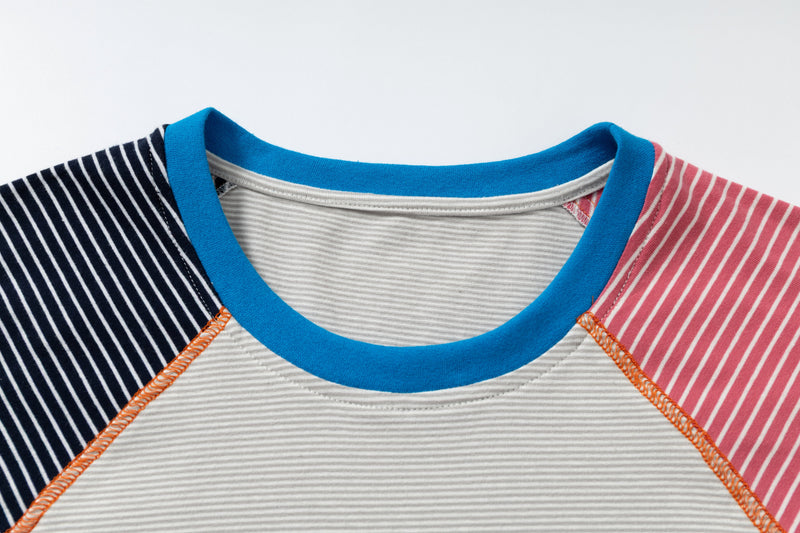 Close-up of a color block raglan T-shirt with navy and pink striped sleeves, bright blue ribbed collar, and relaxed fit