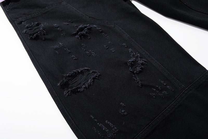 Close-up of black distressed denim leg with ripped patches and frayed holes