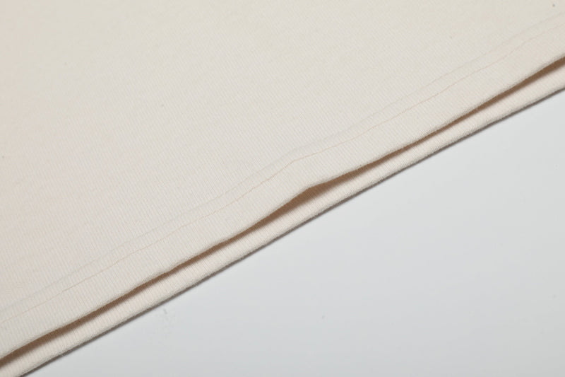 Close-up of cream distressed cotton tee hem with visible stitching and vintage washed texture