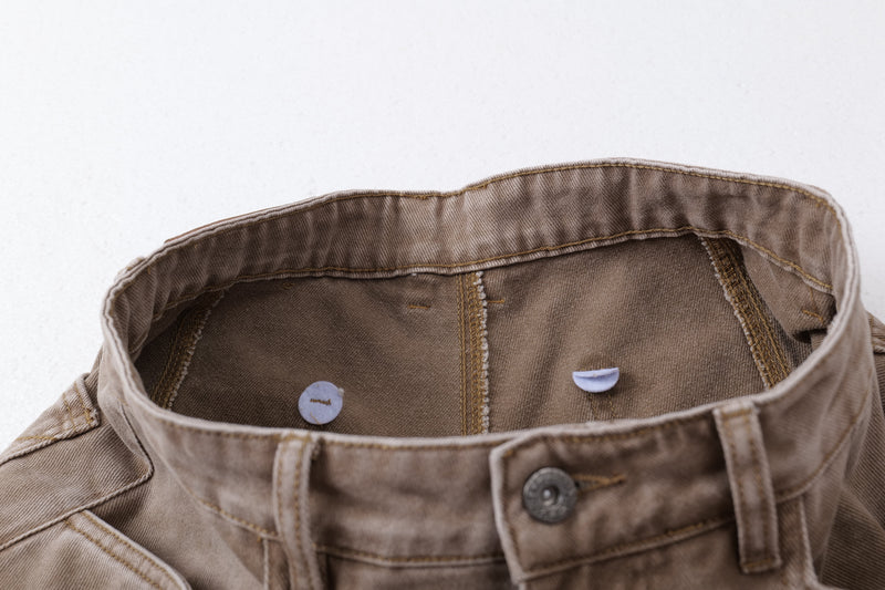 Inside waistband detail of brown jeans with button and stitching