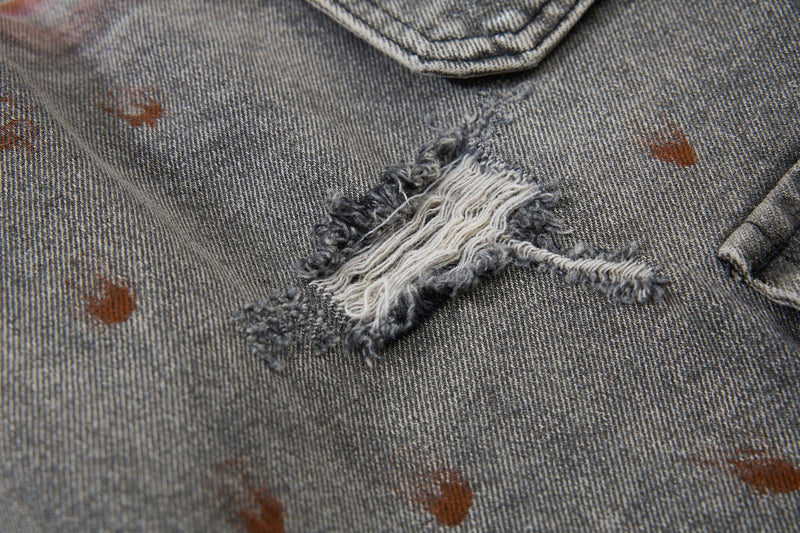 Close-up of a torn denim patch with frayed white threads and brown paint splatter