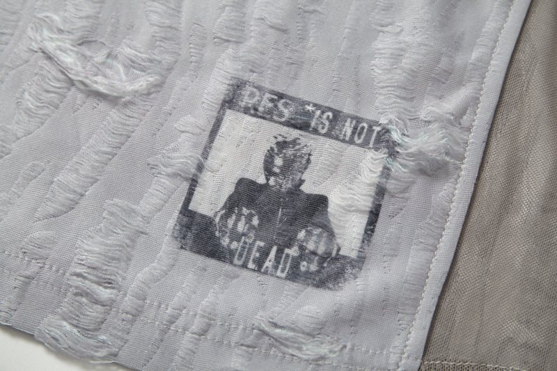 Close-up of a textured white mesh tee with distressed patchwork and faded graphic print detail