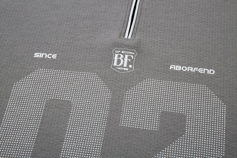 Close-up of gray polo front with zip placket, chest logo, and dotted 02 print