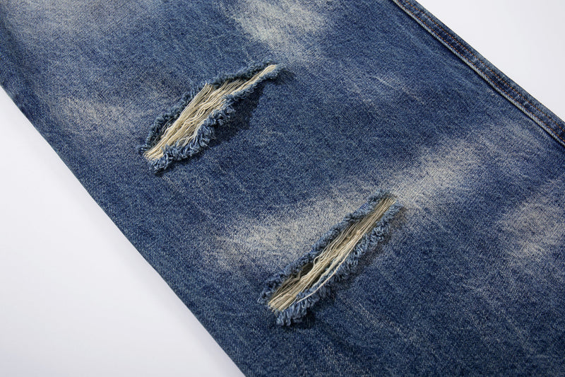 Close-up of ripped denim leg with frayed holes and faded blue wash