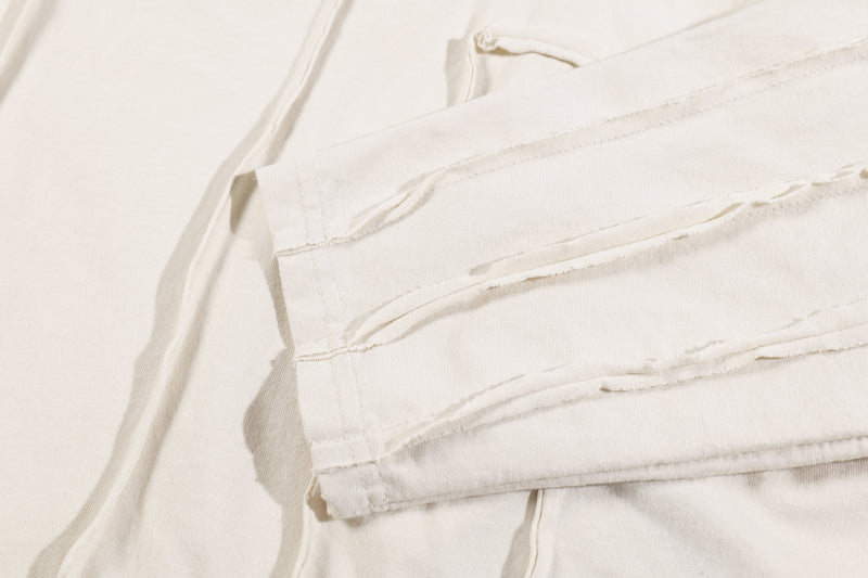 Close-up of cream long sleeve tee sleeve with layered patchwork seam details