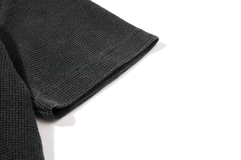 Close-up of a dark gray waffle knit T-shirt sleeve with textured fabric and folded hem on a white background