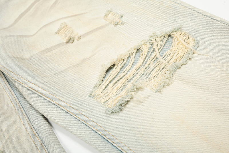 Close-up of large frayed rip on cream denim pant leg