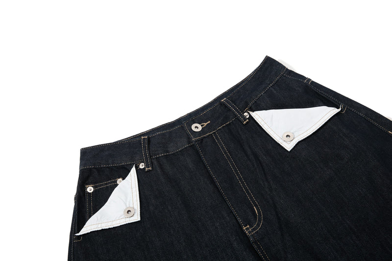 Close-up of the waistband on dark wash denim pants with white contrast pocket flaps and topstitching