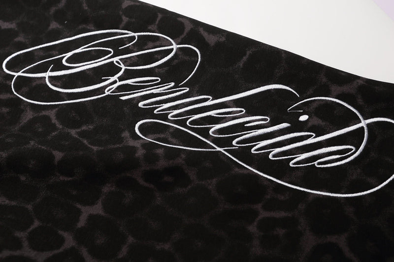 Close-up of white script graphic on black leopard print shorts