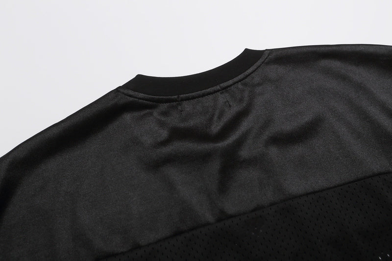 Close-up of a black varsity football jersey T-shirt with ribbed crew neck and perforated mesh paneling on the hem