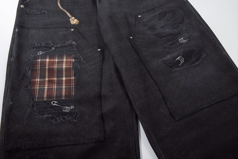 Back leg close-up of black denim pants with patch pocket, plaid panel, and distressed print