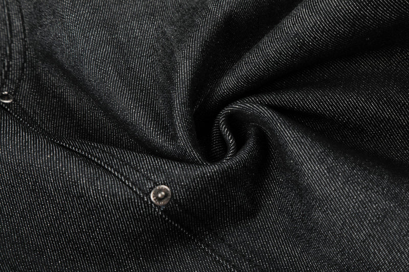 Close-up of black denim fabric texture with stitched seam and metal rivet