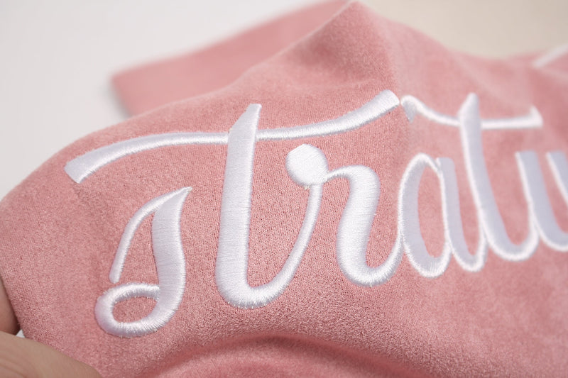 Close-up of a pink suede athletic T-shirt with white embroidered lettering and soft textured fabric