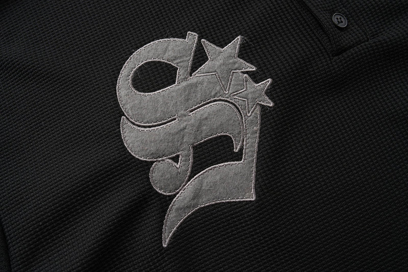 Close-up of gray star patch embroidery on black waffle-knit Henley shirt
