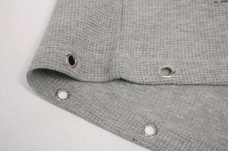 Close-up of a gray waffle knit gothic graphic tee hem with metal grommet details and exposed stitching