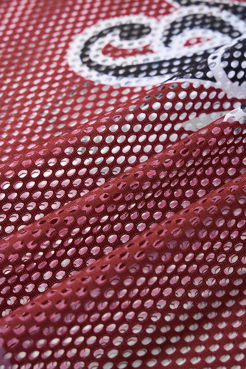 Close-up of maroon mesh jersey fabric with white polka-dot perforations and a varsity-style graphic print