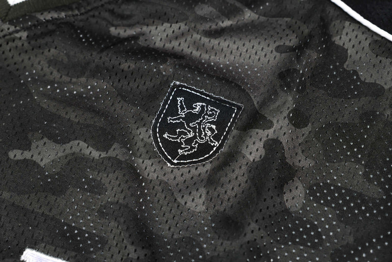 Dark camo mesh athletic jersey with embroidered crest and white trim detail in close-up