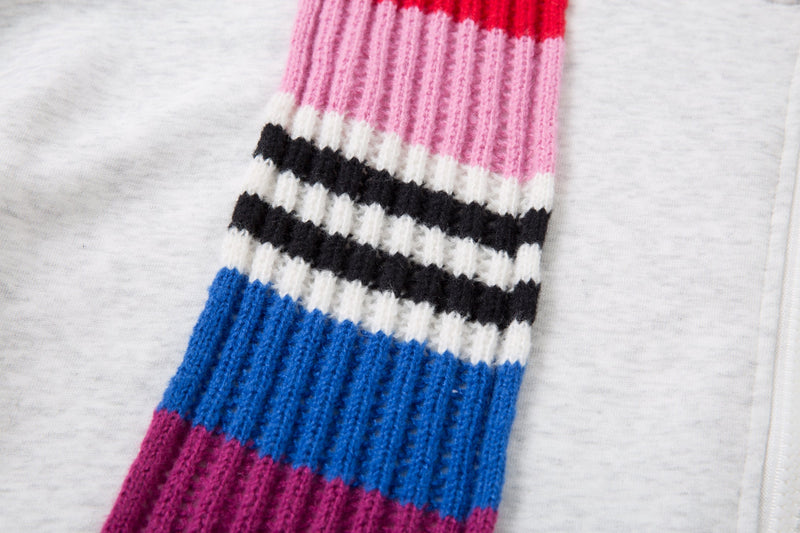 Close-up of a striped knitted scarf panel with pink, black, blue, and red sections on a light gray hoodie