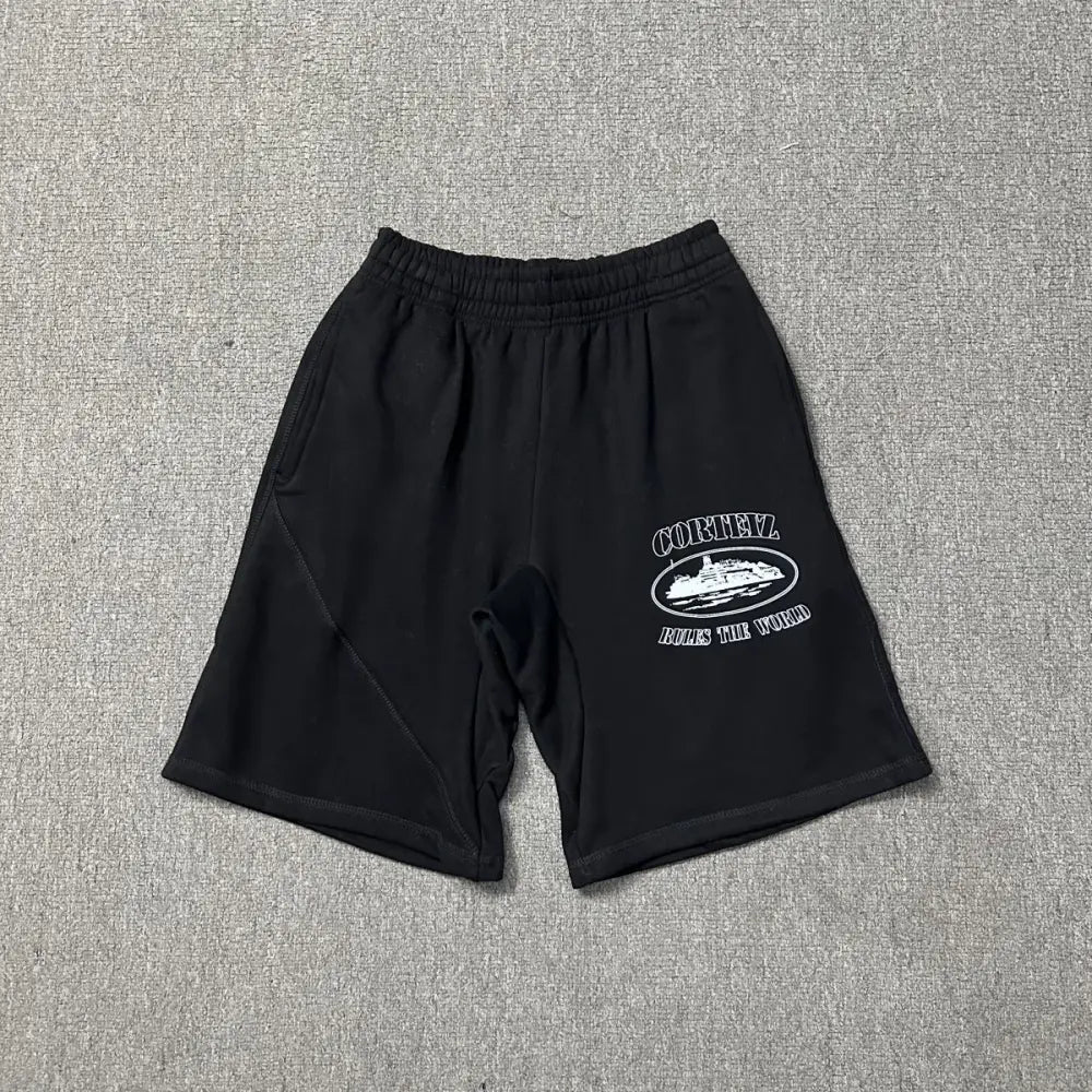 Black Corteiz cotton jogger shorts laid flat, showing white oval graphic print on the front leg reading Corteiz Rules the World