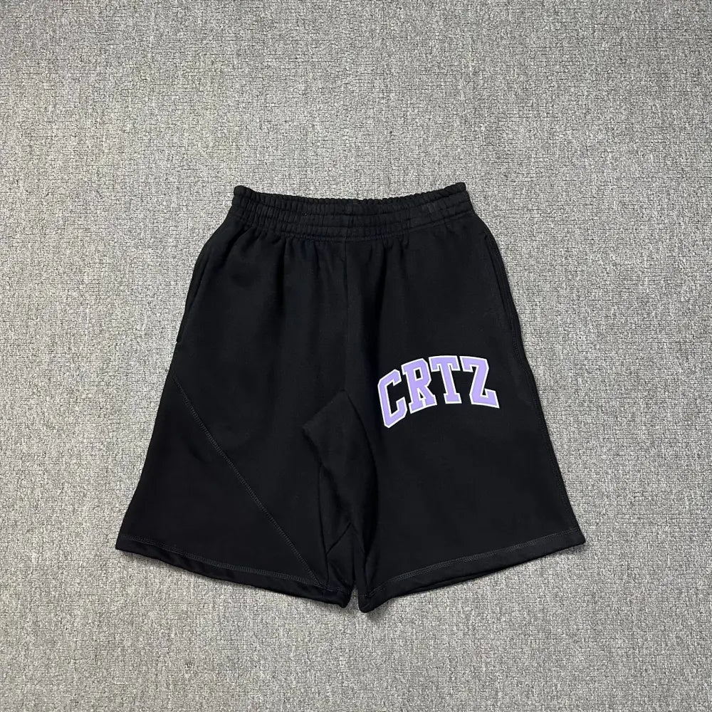 Black Corteiz jogger shorts laid flat, showing purple arched CRTZ letter print on the front left leg and elasticated waistband