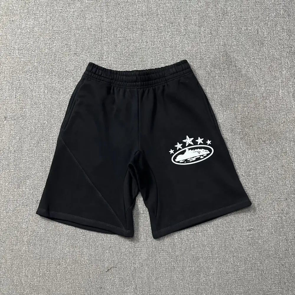 Black Corteiz cotton shorts laid flat, showing white star and oval logo graphic print on the left leg
