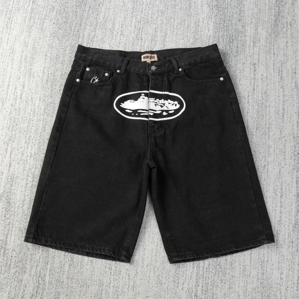 Black Corteiz denim shorts laid flat, showing a large white oval graphic print on the front and a small embroidered logo on the left coin pocket