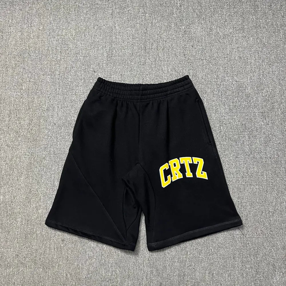 Black Corteiz jogger shorts laid flat, showing yellow arched CRTZ letter print on the front and elasticated waistband