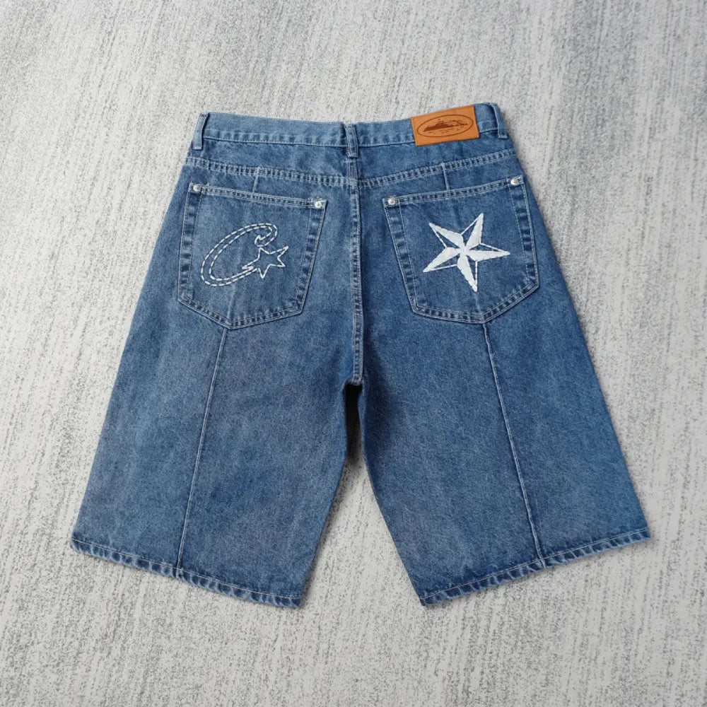 Back view of Corteiz blue denim shorts laid flat, showing large white star embroidery on the right back pocket and Corteiz C logo embroidery on the left back pocket