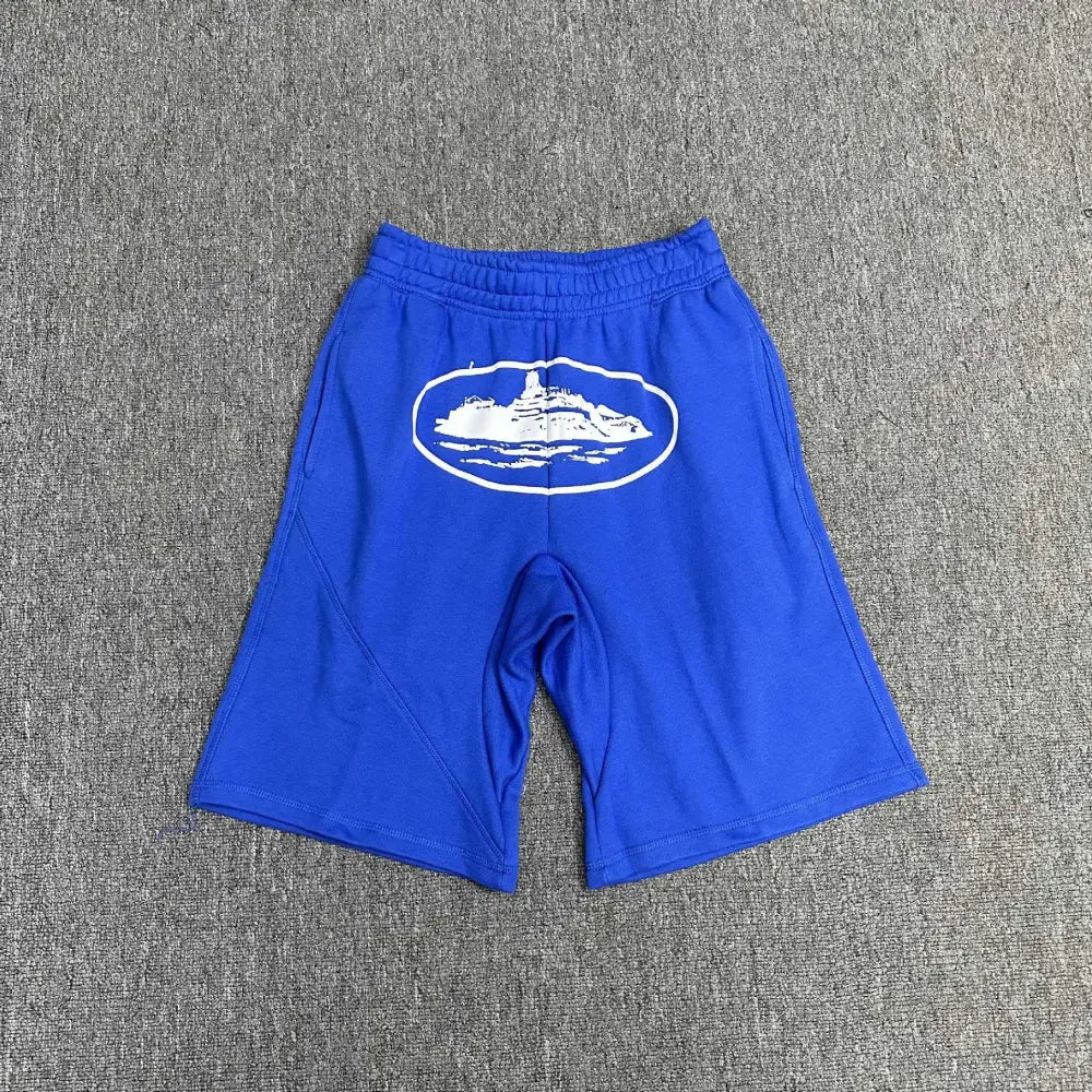 Blue Corteiz cotton jogger shorts laid flat, showing a large white oval graphic logo print on the front