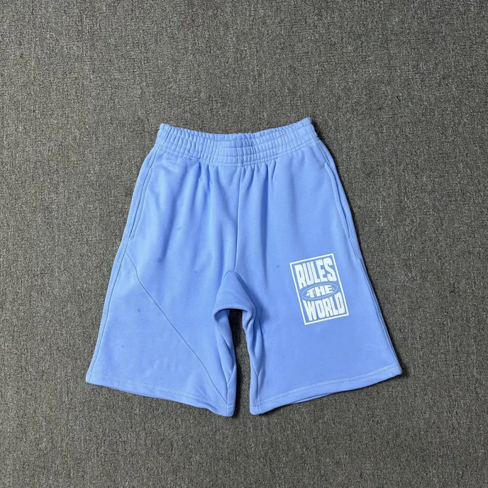 Light blue Corteiz cotton shorts laid flat, showing white Rules The World graphic print on the left leg