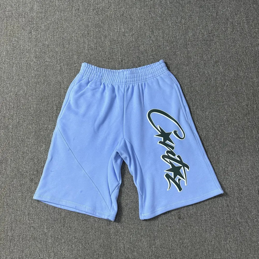 Light blue Corteiz cotton jogger shorts laid flat, showing large script logo and star print on the front leg