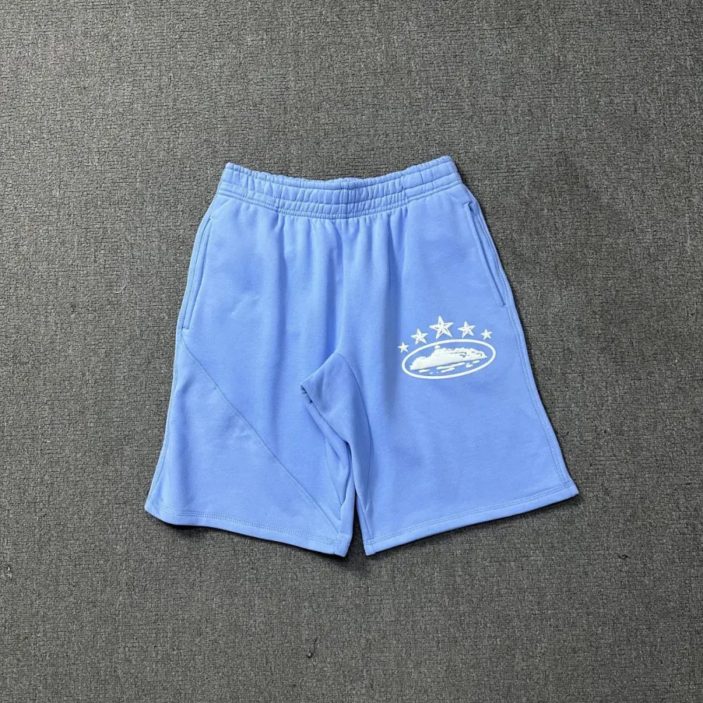 Light blue Corteiz cotton shorts laid flat, showing white globe and star graphic printed on the left leg