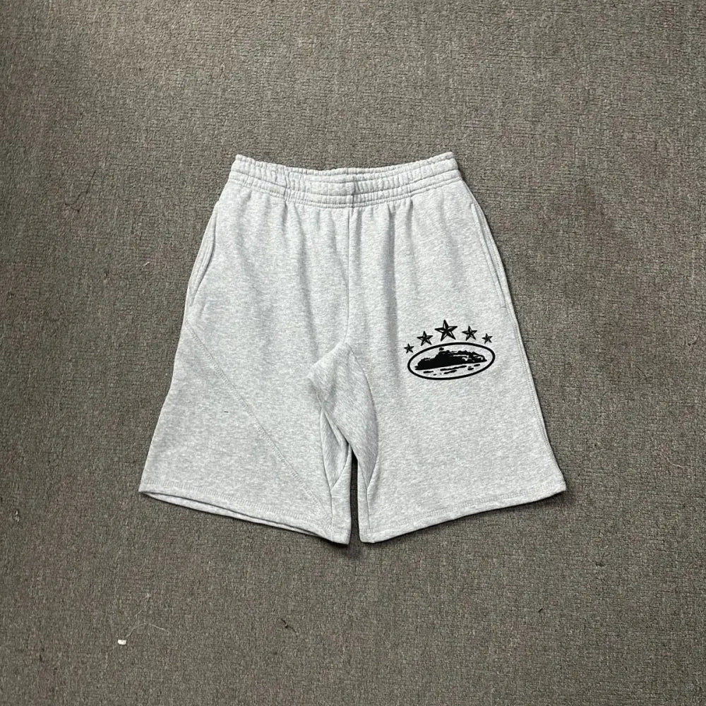 Light grey Corteiz cotton jogger shorts laid flat, showing a black star and oval logo graphic printed on the left leg