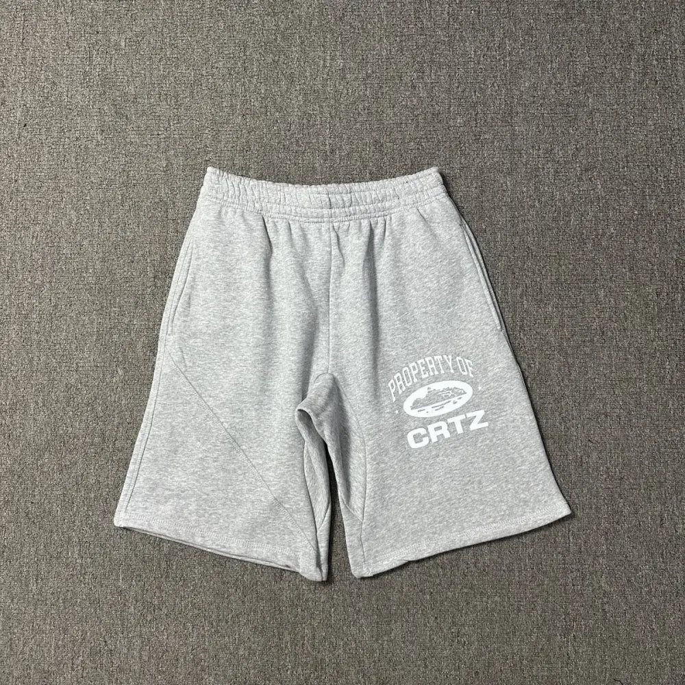 Light grey Corteiz cotton shorts laid flat, showing white Property of CRTZ graphic print on the left leg
