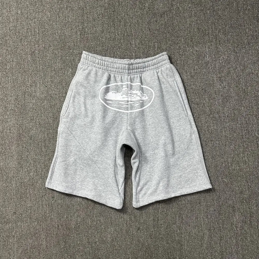 Light grey Corteiz cotton shorts laid flat, showing a white oval graphic print on the front panel and elasticated waistband