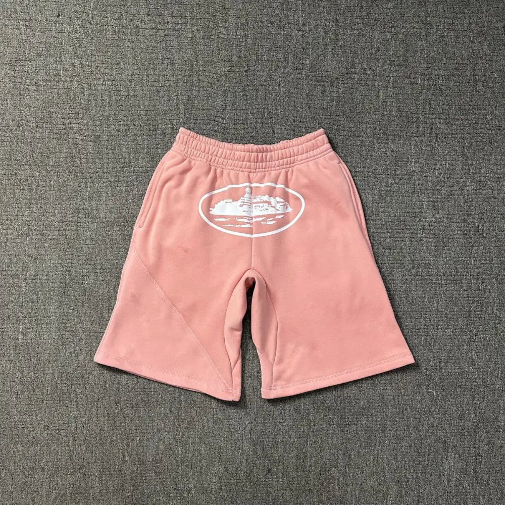 Pink Corteiz cotton shorts laid flat, showing white oval graphic print on the front and elasticated waistband