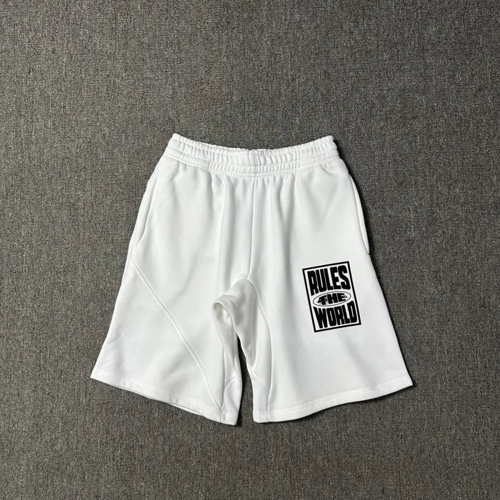 White cotton jogger shorts laid flat, showing a black Rules The World graphic print on the left leg and an elasticated waistband