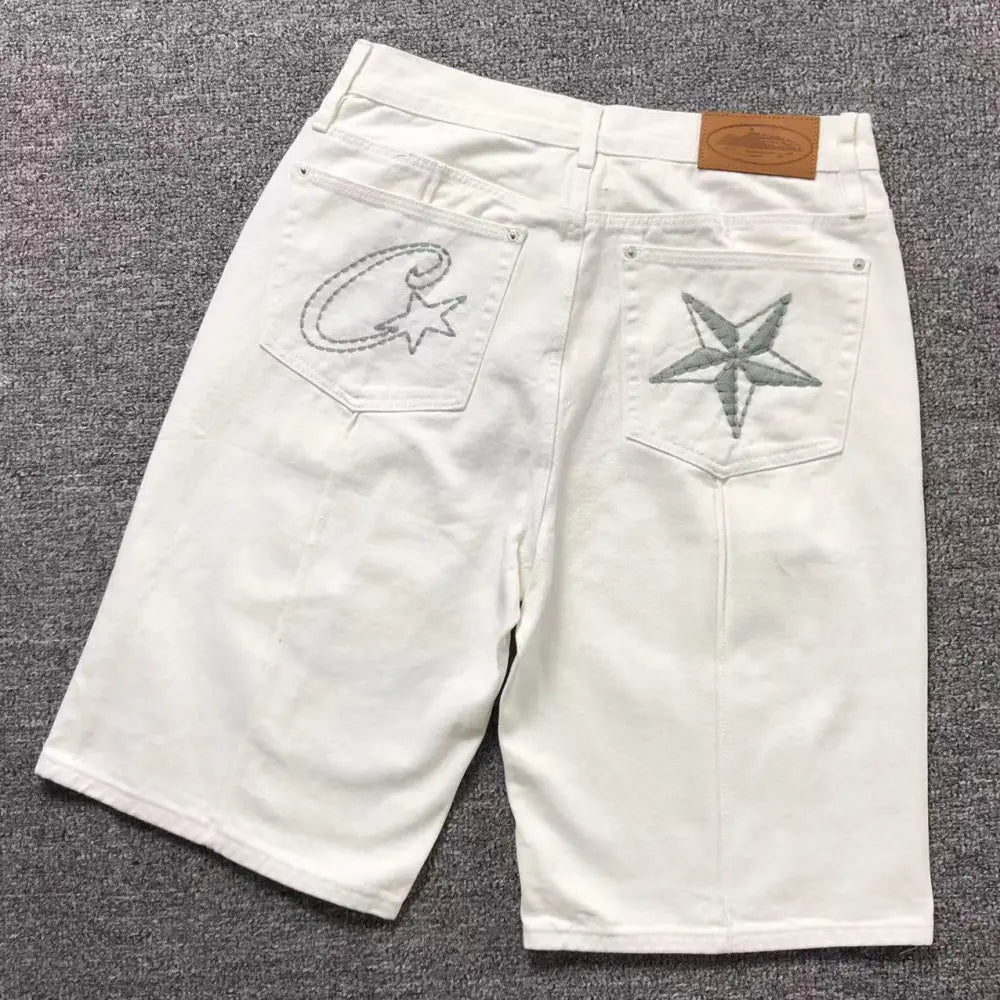 Back view of white Corteiz denim shorts laid flat, showing embroidered logo and star on back pockets with leather waistband label