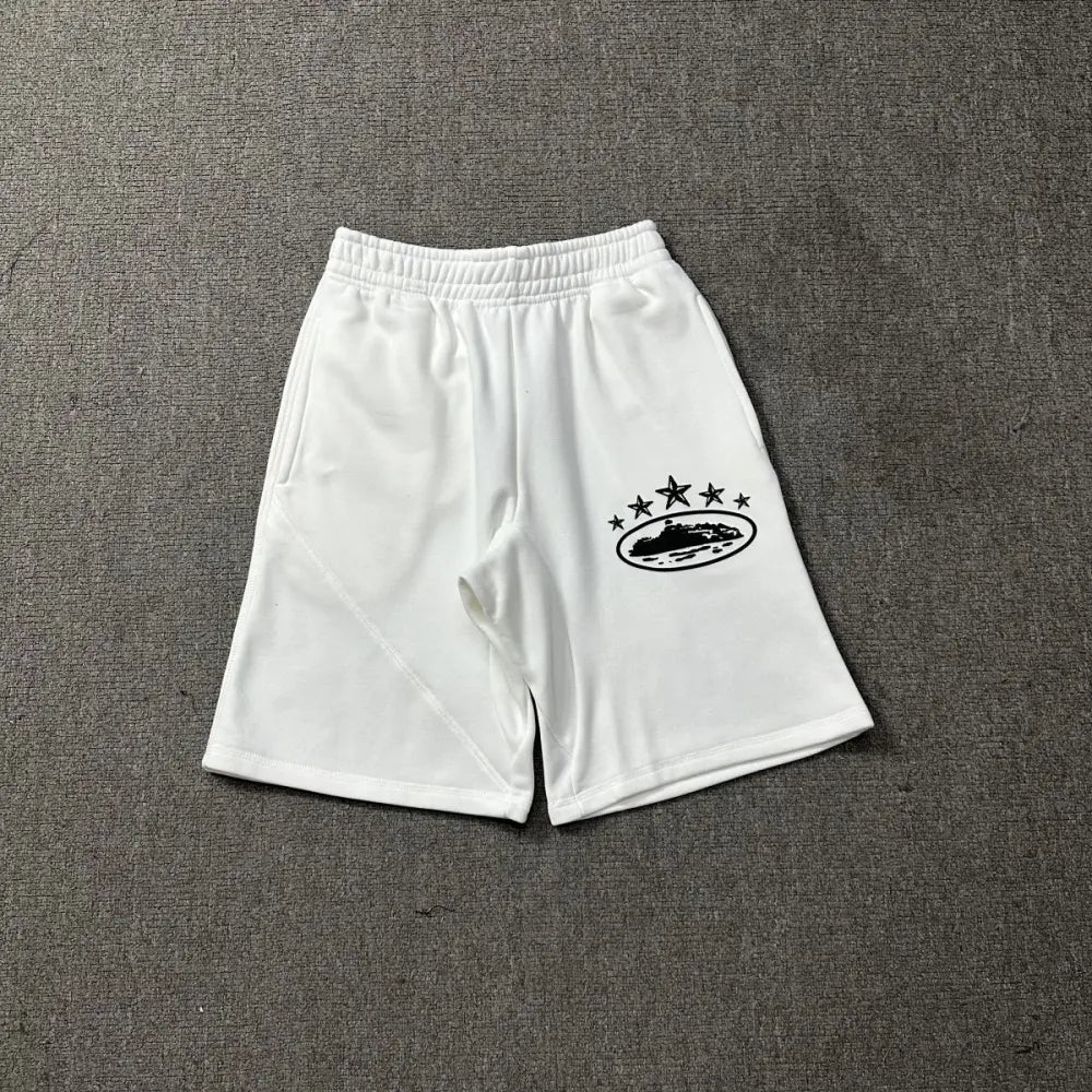 White Corteiz cotton jogger shorts laid flat, showing a black star and oval logo graphic printed on the front leg