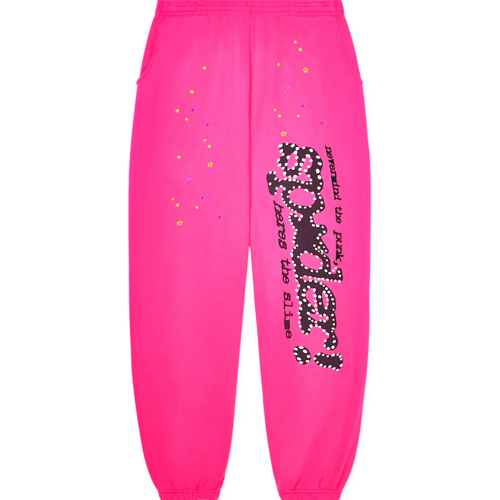 The Sp5der Sweatpants are unisex pink cotton wide leg sweatpants featuring a bold graphic logo print on the left leg with "spider!" in black and white bubble letters, colorful stars, extra black text, and elastic waistband and cuffs.