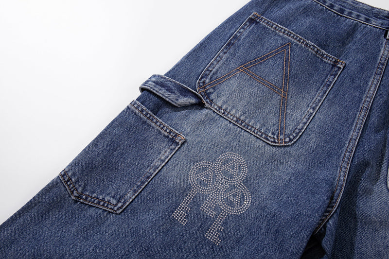 Side close-up of blue carpenter jeans showing patch pocket, folded cuff, and rhinestone key graphic