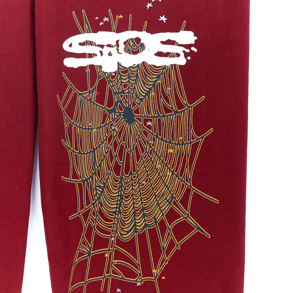 The Sp5der Sweatpants are unisex burgundy cotton sweatpants featuring a large yellow spider web graphic, white graffiti-style text, and small white stars—perfect for bold streetwear looks.