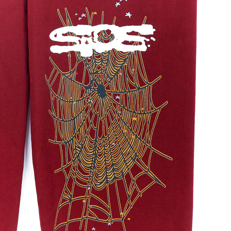 The Sp5der Sweatpants are unisex burgundy cotton sweatpants featuring a large yellow spider web graphic, white graffiti-style text, and small white stars—perfect for bold streetwear looks.