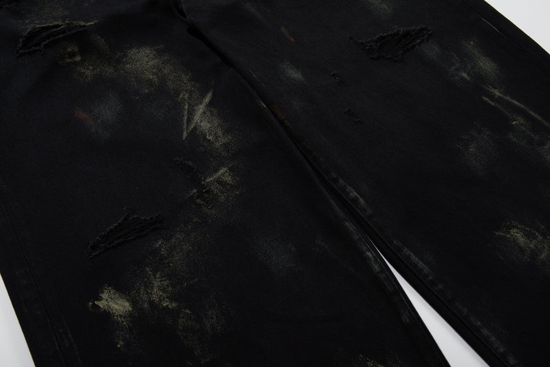 Close-up of distressed black denim fabric with paint-wash marks and frayed rips