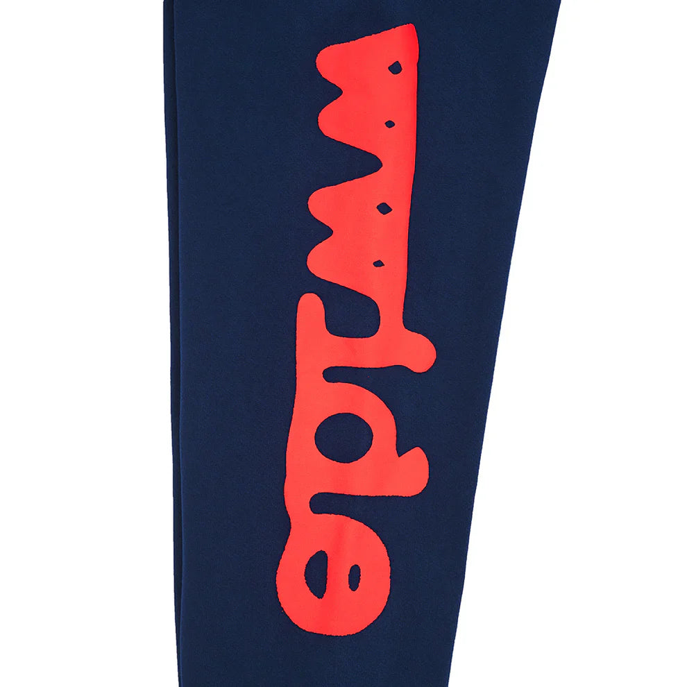 A close-up of the Sp5der Sweatpants Navy Blue Red Side Logo Print—100% cotton streetwear jogger pants—shows bold, wavy red lettering running vertically along the navy blue fabric.
