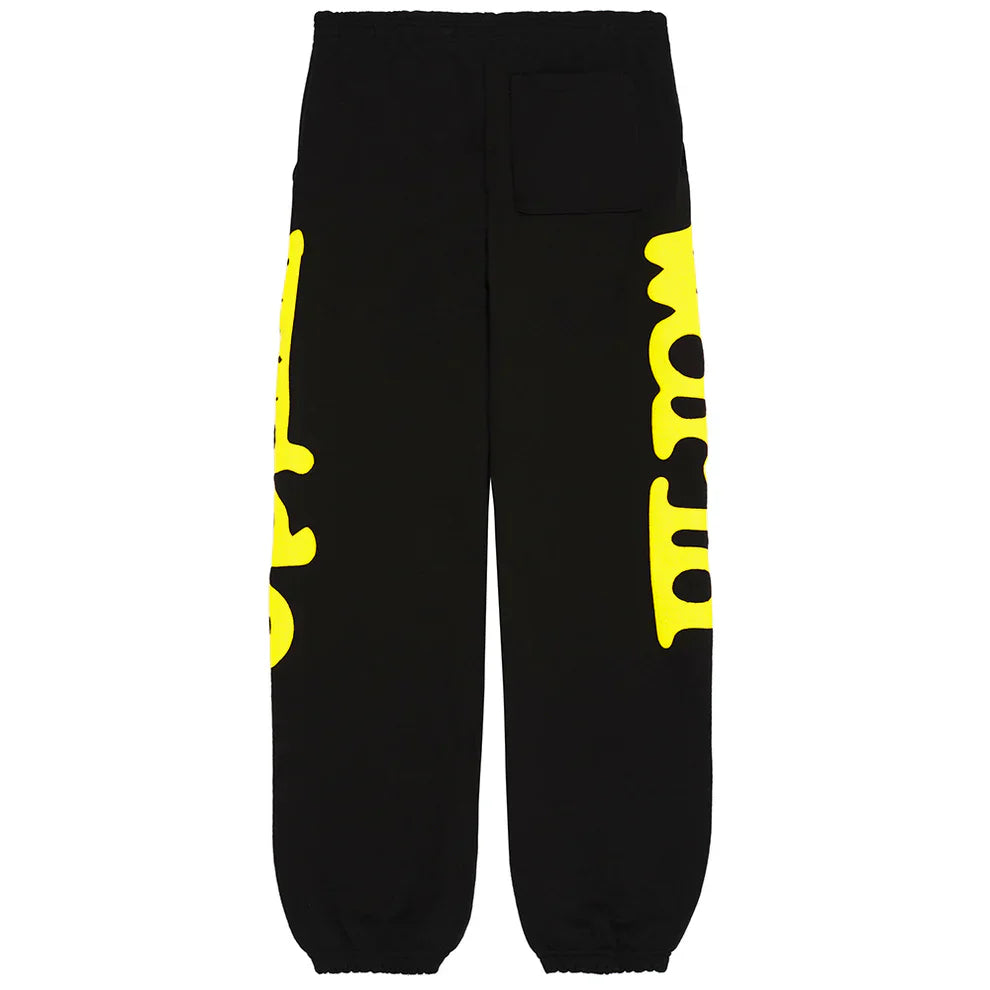 The Sp5der Sweatpants Black Yellow Side Logo Print are 100% cotton streetwear jogger pants with elastic cuffs, a back pocket, and bold yellow graphics featuring stylized, partially cut-off text running down both legs for an edgy look.