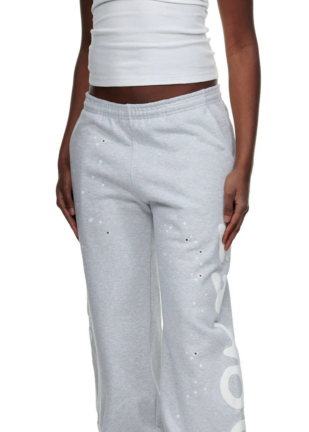 A person stands against a plain background wearing a white ribbed tank top and 100% Cotton Sp5der Sweatpants for Men—Grey Streetwear Jogger Pants with Graphic Print and relaxed fit, showcasing laid-back streetwear style.