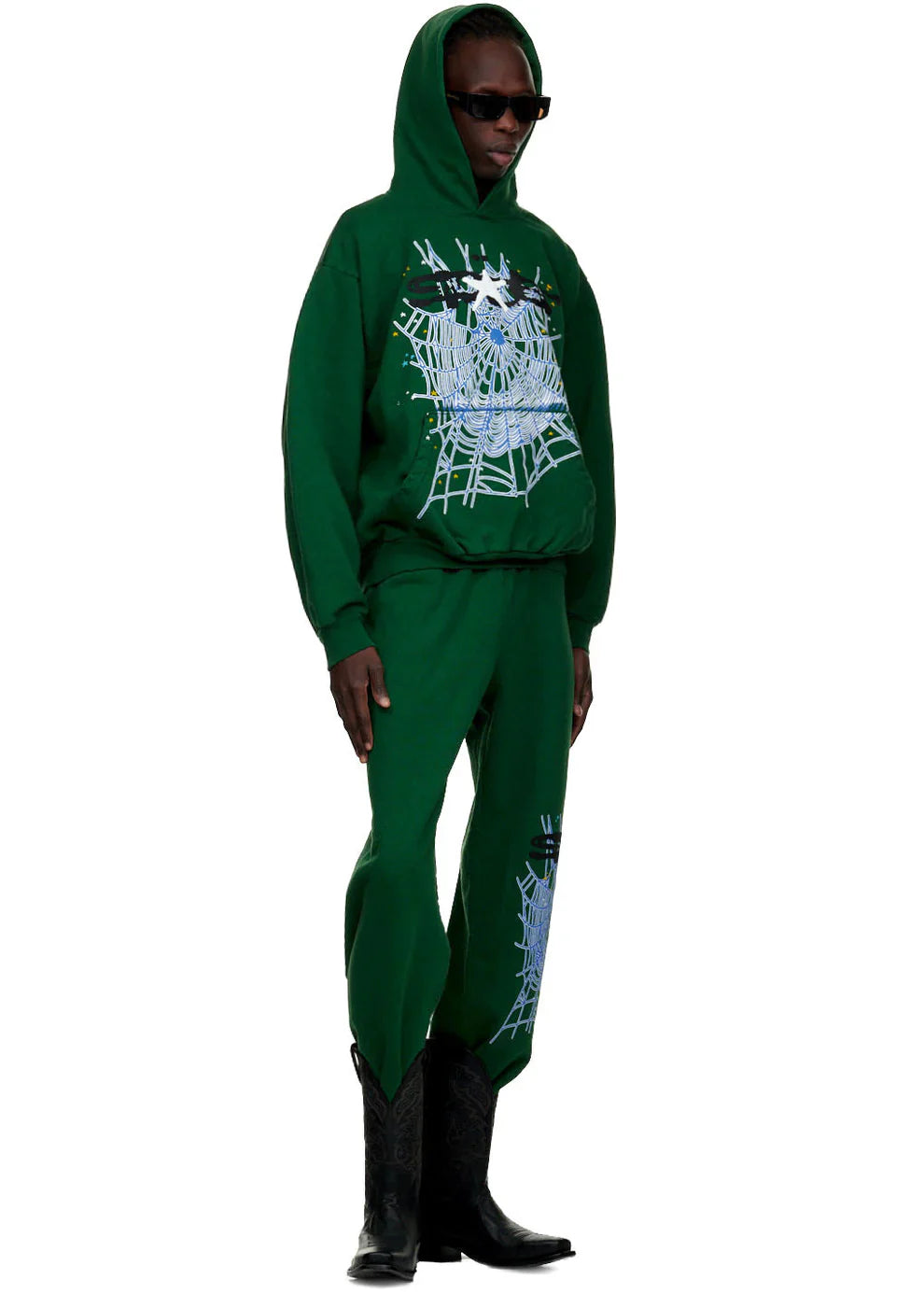 A person stands against a white background wearing black sunglasses, black cowboy boots, and 100% Cotton Sp5der Sweatpants for Men—Dark Green Streetwear Jogger Pants with Spider Web Graphic, Relaxed Fit.