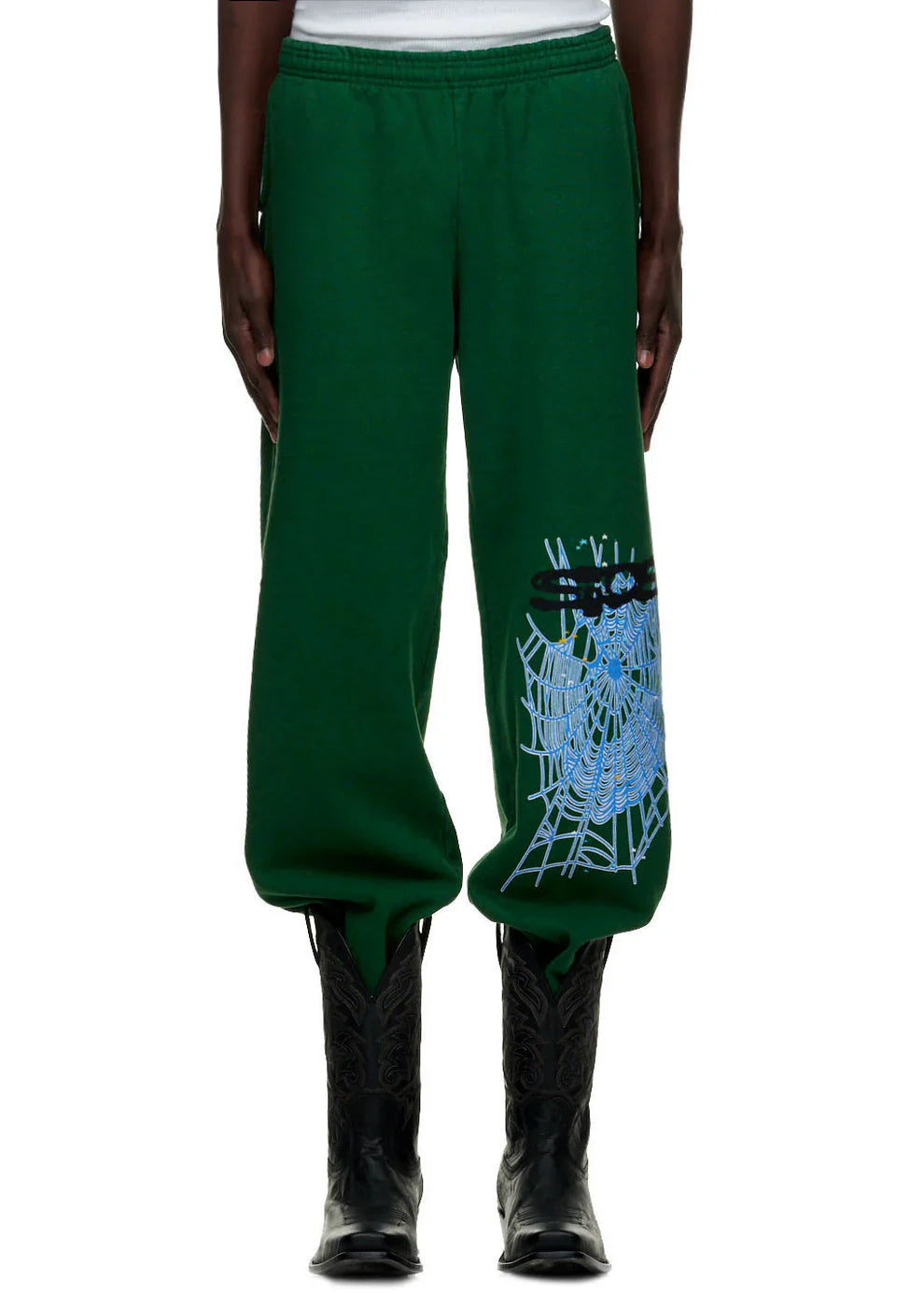 A person wearing 100% Cotton Sp5der Sweatpants for Men – Dark Green Streetwear Jogger Pants with Spider Web Graphic, paired with black cowboy boots and a white top.